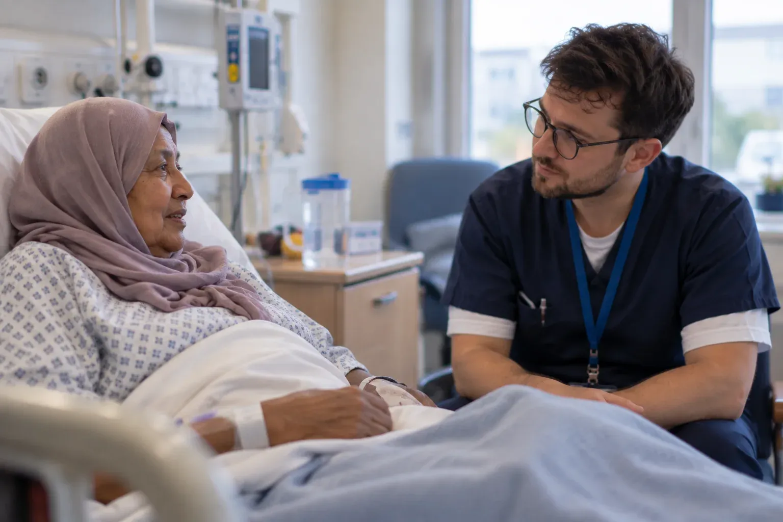 A nurse sitting at a patient’s bedside, talking with her at eye level.