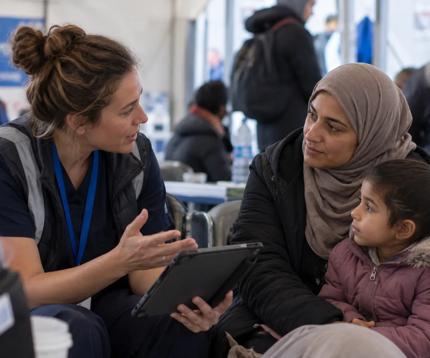 A health worker using CardMedic on a tablet with a mother and child in a humanitarian health setting.